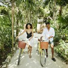 Wide shot of smiling couple walking bikes on pathway in jungle at tropical resort
1366306661
exotic travel
A woman and man walking along a path with bikes in Mexico