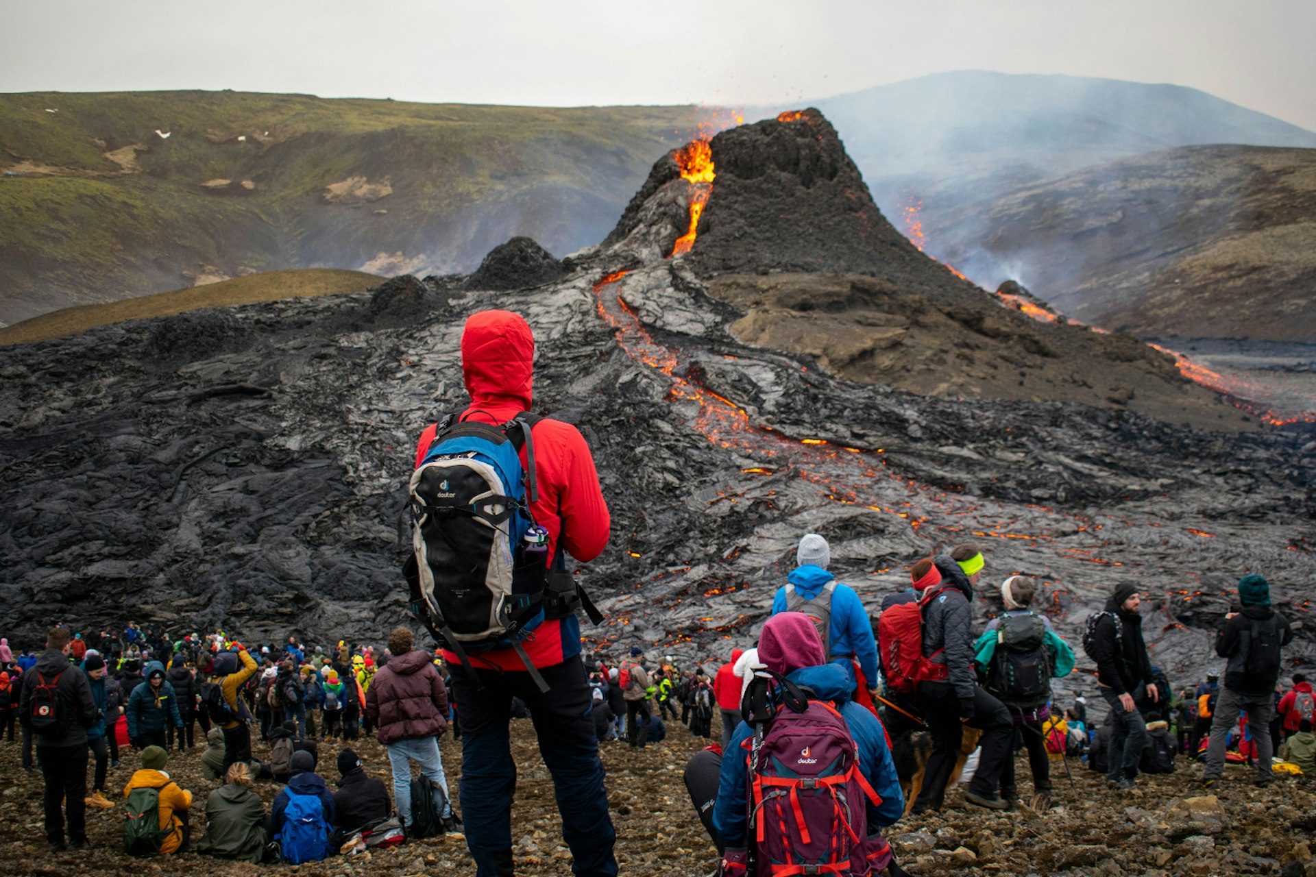 An Iceland volcano erupts while a group of travelers watches it from a distance