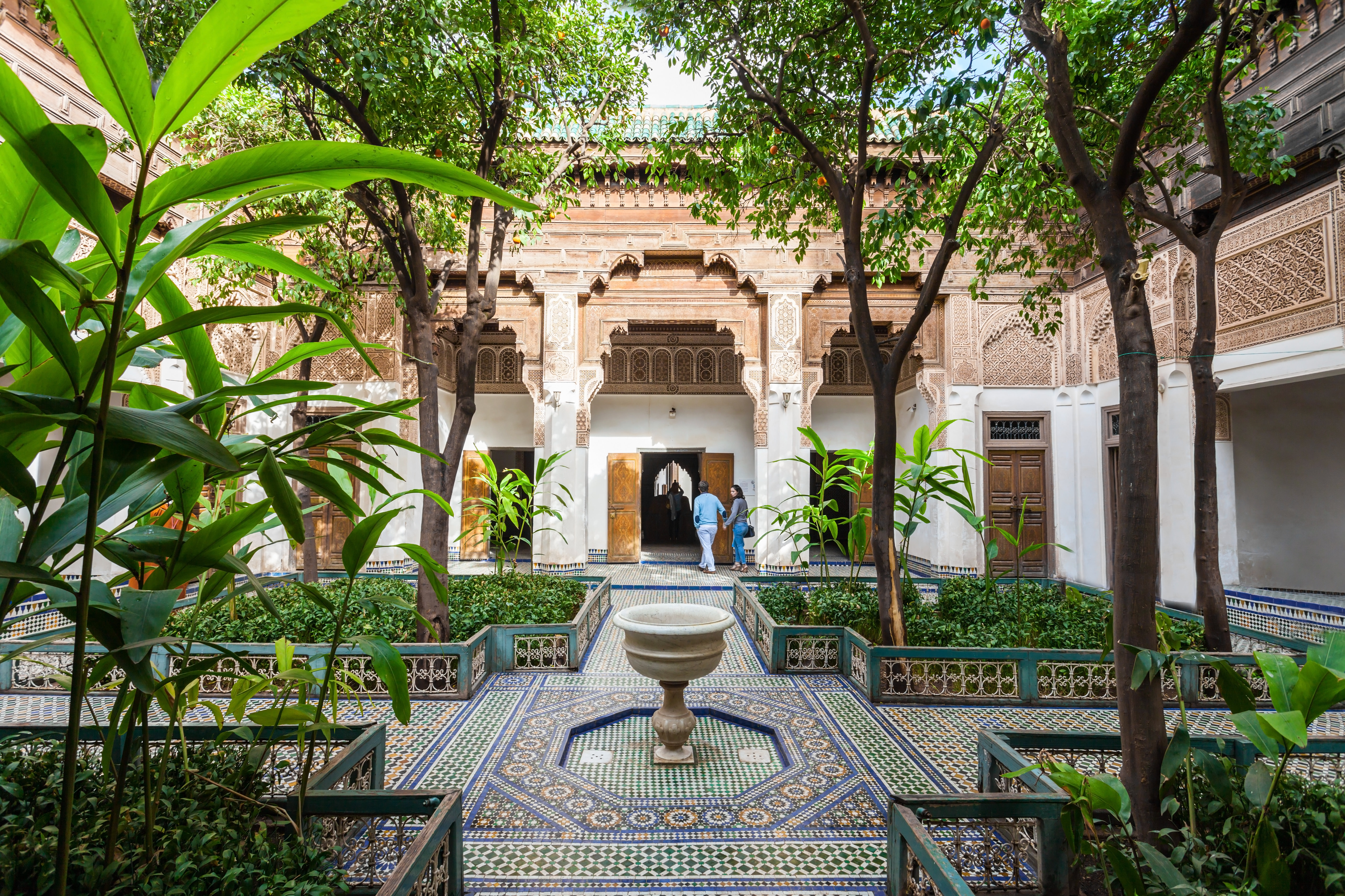 A grand, tiled courtyard with a number of raised flower beds, from which large leafy trees grow.